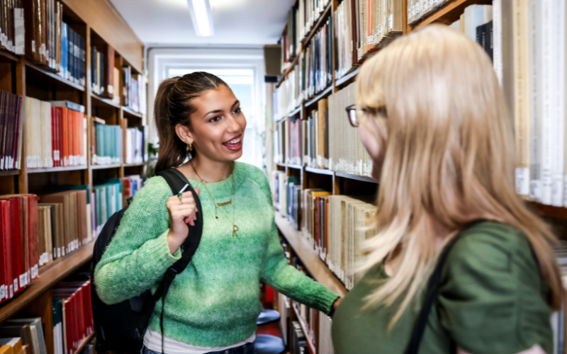 Image shows two students in converation at the UCL library