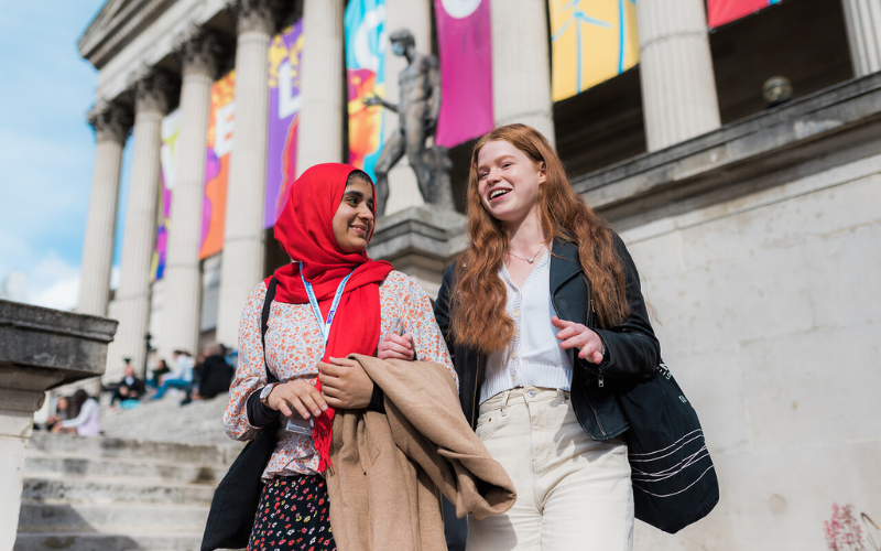 Image shows two students walking outside the Welcome to UCL sign