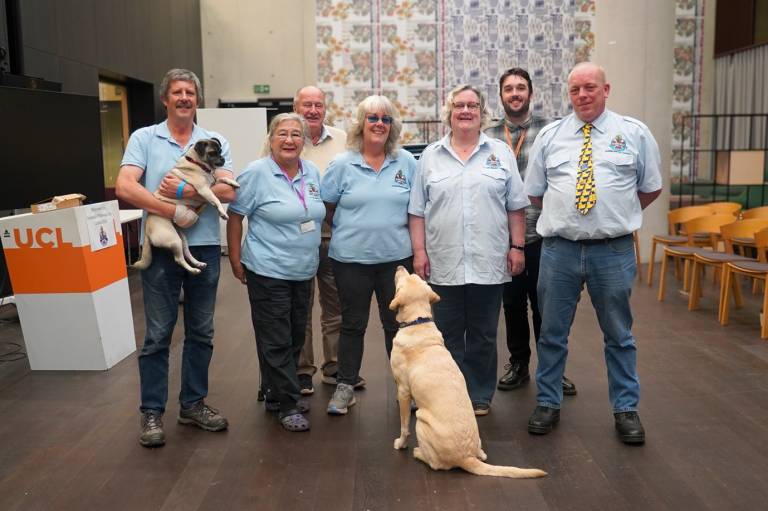 A group of people face the camera standing in a line with a service dog looking up at them in the middle of the picture