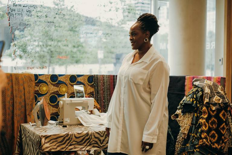 Person stand infront of window, and draped between them and the winder are brightly coloured African print fabrics.