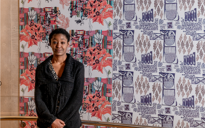 Abi Ola stood in front of her wallpaper print work in a black cardigan.