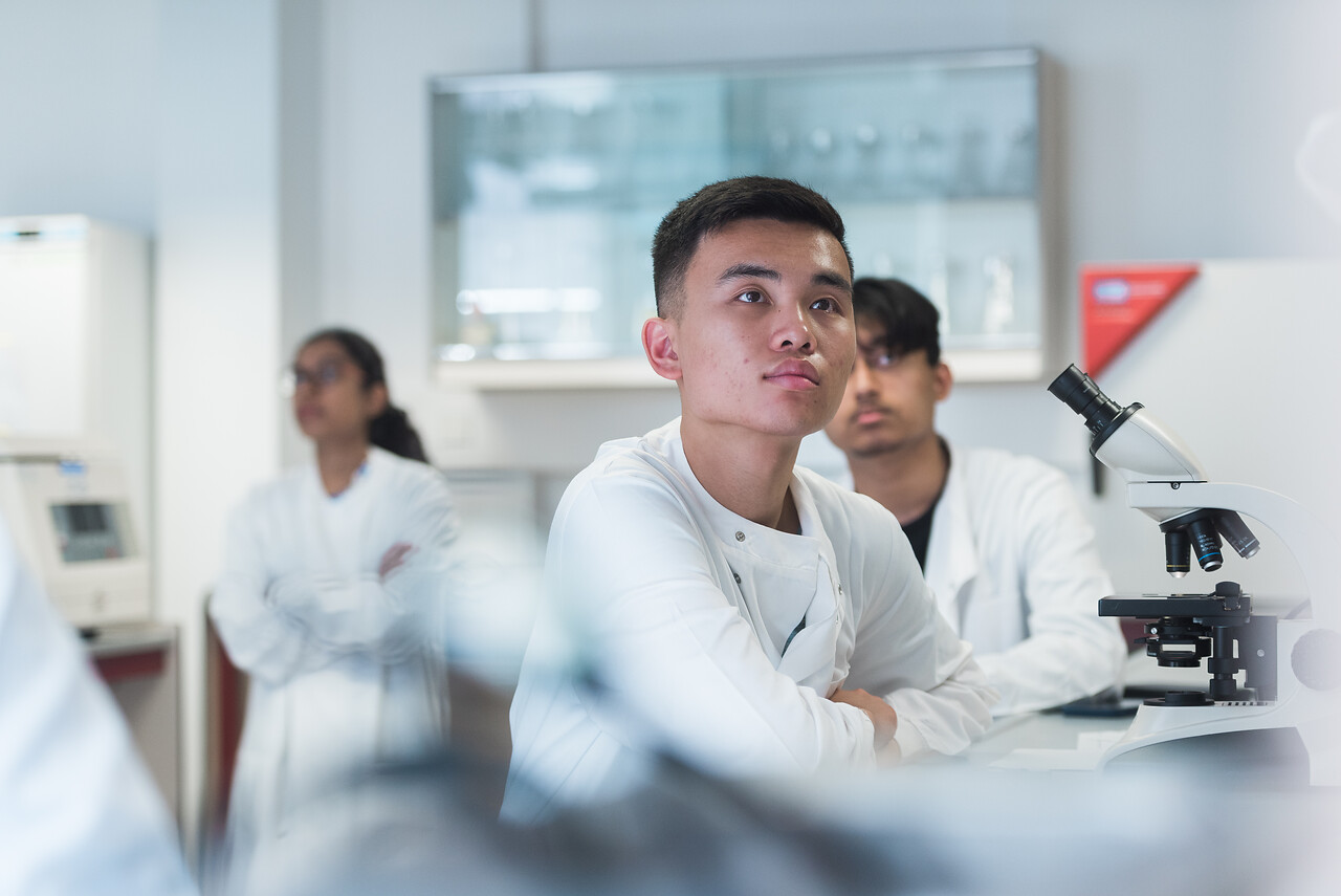 student in a lab coat listens to lecturer in laboratory